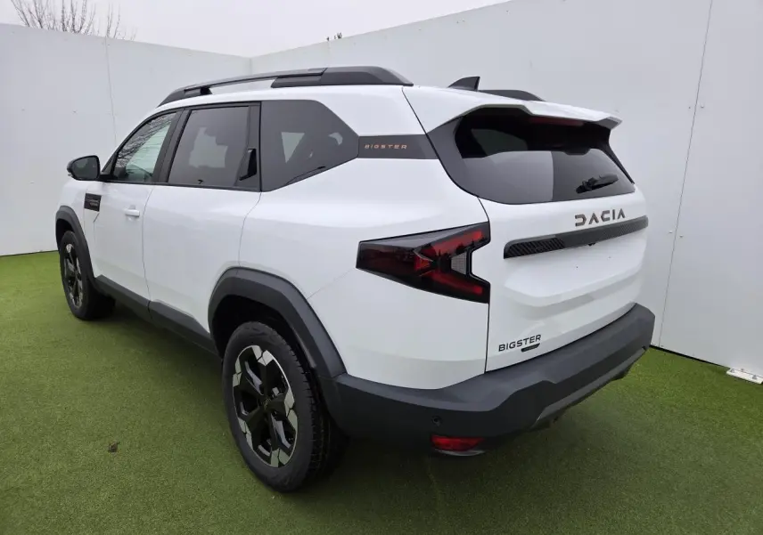Vue 3/4 arrière droite du Dacia Bigster blanc glacier avec jantes alliage et détails brun cuivré sur fond vert.