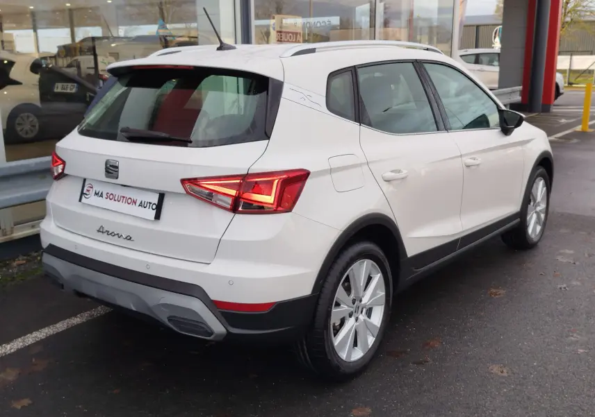 Vue 3/4 arrière droite d'un SEAT Arona blanc Candy 2023 avec feux LED et jantes alliage visibles.