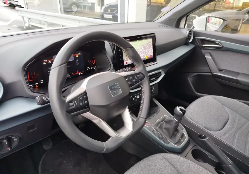 Vue intérieure côté conducteur du tableau de bord et volant du SEAT Arona blanc avec écran tactile et levier de vitesses manuel.