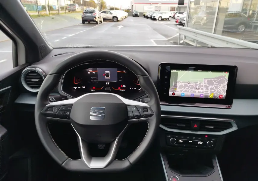 Vue intérieure centrée sur le volant et le tableau de bord numérique d'une SEAT Arona 2023 avec écran tactile et navigation affichée.