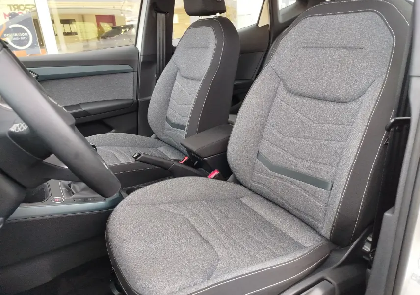 Vue intérieure des sièges avant en tissu gris de la SEAT ARONA 2023, avec accoudoir central et ceintures visibles.