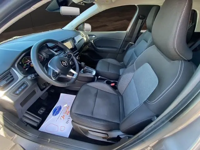 Vue intérieure côté conducteur du Renault Captur E-Tech Full Hybrid 145 gris Cassiopée, sièges tissu noir et tableau de bord moderne.