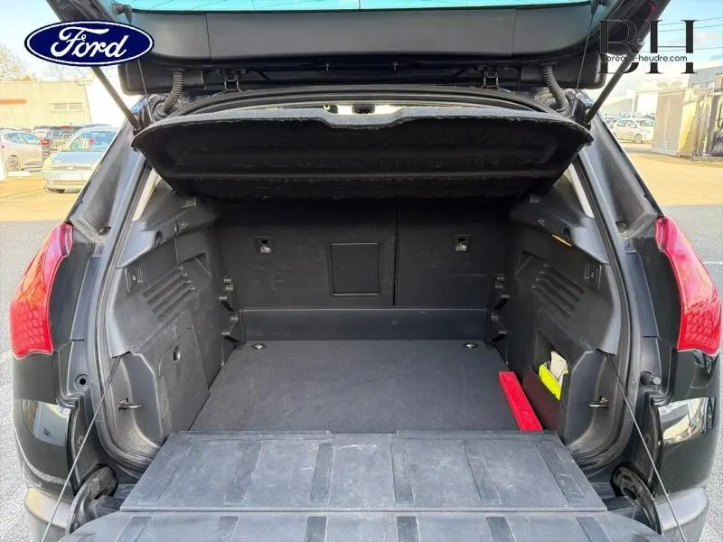 Coffre ouvert vu de l'arrière d'un Peugeot 3008 noir Perla Nera avec banquette rabattue et espace de rangement visible.