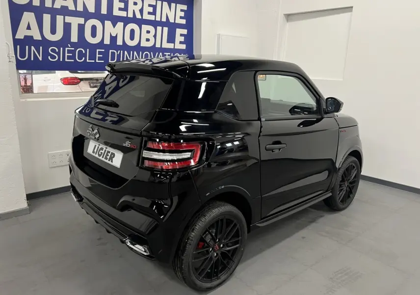 Vue 3/4 arrière droite d'une Ligier JS50 noire mate avec jantes alu noires et feux LED, en intérieur showroom.