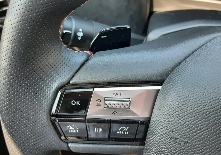 Gros plan sur la partie gauche du volant en cuir noir perforé du DS4 2024, avec commandes de régulateur et assistance visibles.