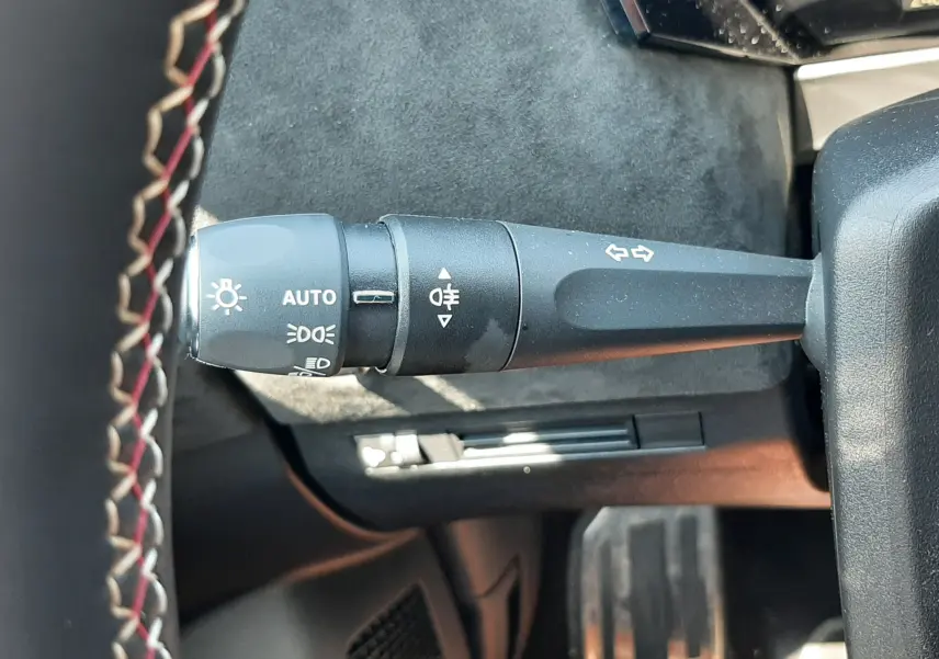 Gros plan sur la manette de clignotants et feux avec marquages blancs, volant cuir noir surpiqûres rouges visible.