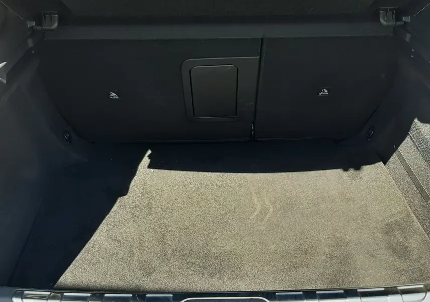 Coffre ouvert d'une DS4 2024 Cristal Pearl, montrant un espace de chargement propre avec tapis noir et accès arrière rabattable.