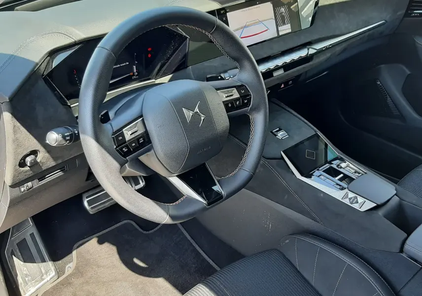 Intérieur noir du DS4 2024, vue du poste de conduite avec volant DS, tableau de bord digital et console centrale moderne.