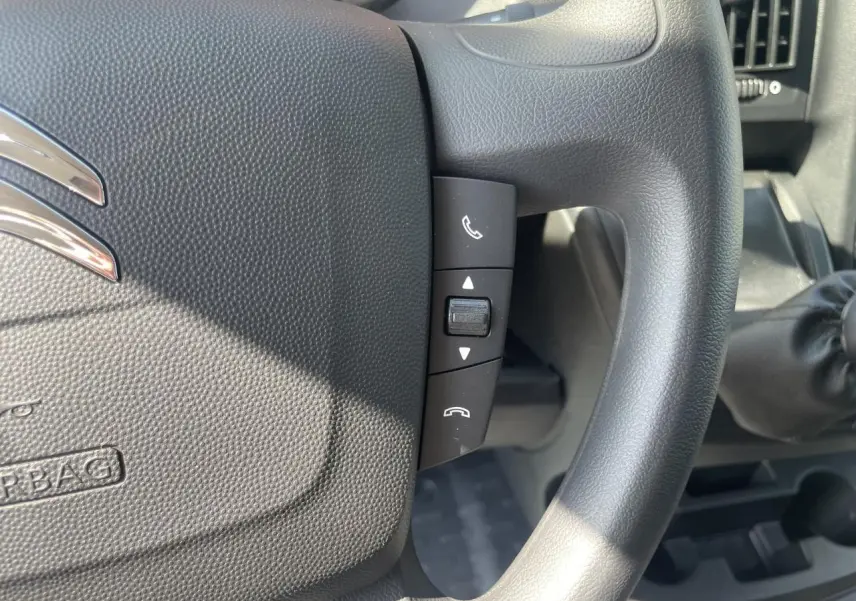Gros plan sur les commandes Bluetooth du volant noir du Citroën Jumper 2023 avec levier de vitesse manuel visible à droite.