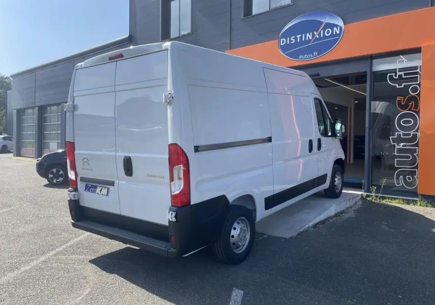 Vue 3/4 arrière droite d'un utilitaire Citroën Jumper blanc stationné devant un garage avec portes arrière tôlées ouvertes à 270°.