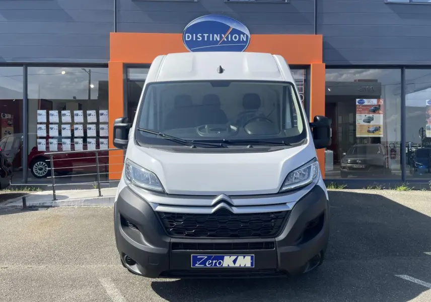 Vue de face d'un utilitaire Citroën Jumper blanc avec calandre noire et plaque Zero KM devant un showroom.