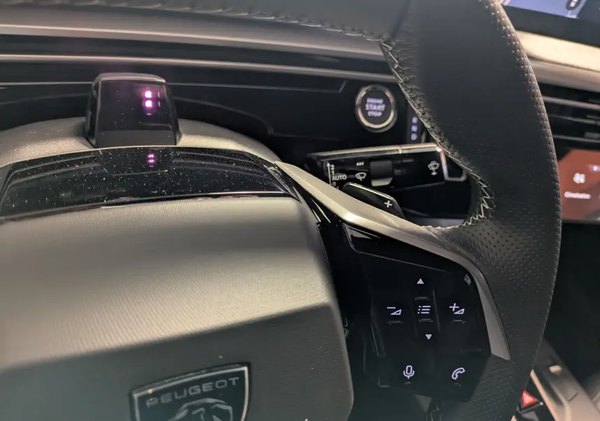 Gros plan sur le volant noir perforé du Peugeot 3008 blanc, avec commandes intégrées et bouton Start/Stop visible.