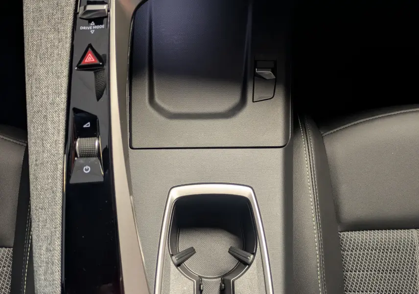 Vue plongeante sur la console centrale noire du Peugeot 3008 hybride 2026 avec porte-gobelets et commandes tactiles.