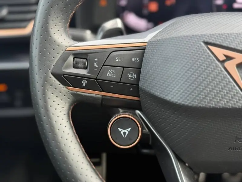 Gros plan sur le volant perforé du CUPRA Formentor blanc Nevada, avec commandes multifonctions et logo cuivre distinctif.