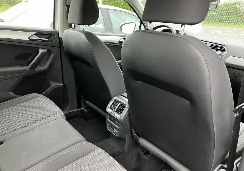 Vue intérieure arrière du Volkswagen Tiguan blanc 2018, montrant les sièges avant en tissu noir et les aérateurs arrière.