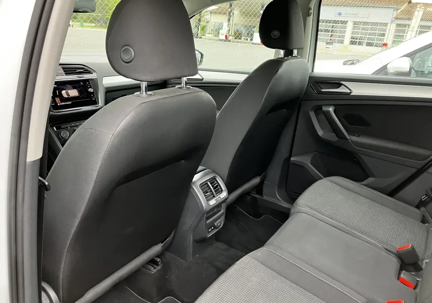 Vue intérieure arrière du Volkswagen Tiguan blanc 2018, sièges noirs en tissu et console centrale avec aérateurs et ports USB.