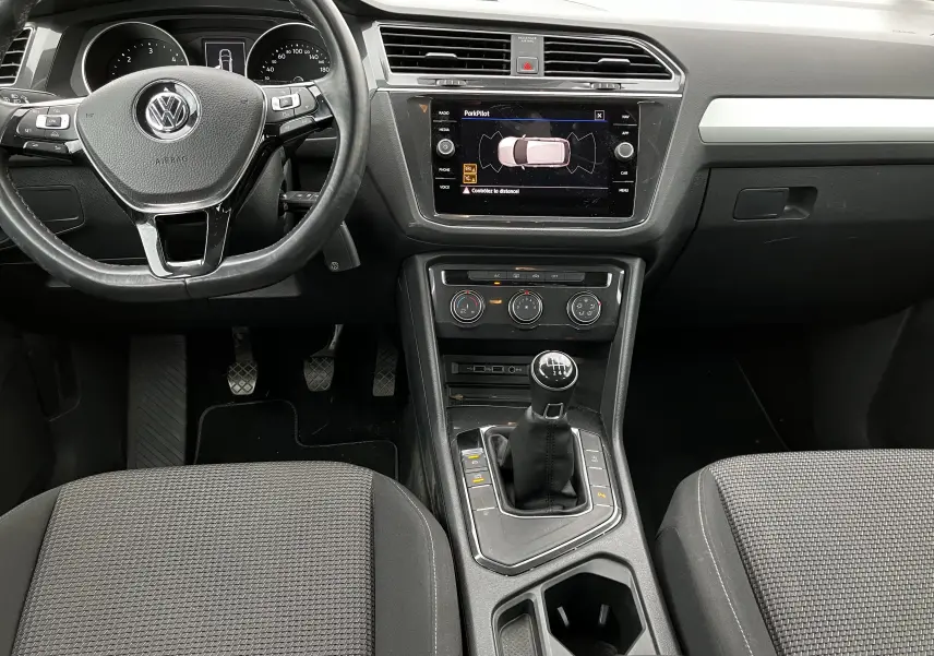 Vue intérieure avant du Volkswagen Tiguan blanc 2018, mettant en valeur le volant multifonction et la boîte manuelle six vitesses.