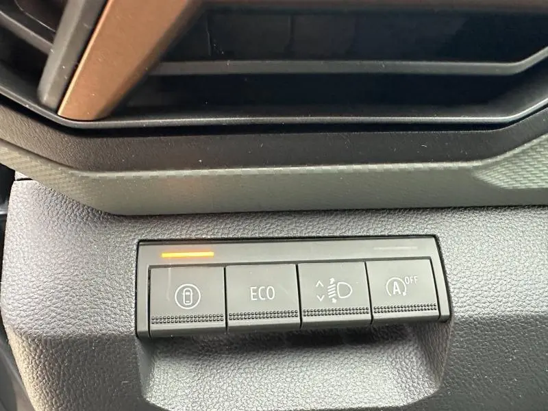 Gros plan sur les boutons de commande noir du tableau de bord du Dacia Duster blanc, avec témoin orange allumé.