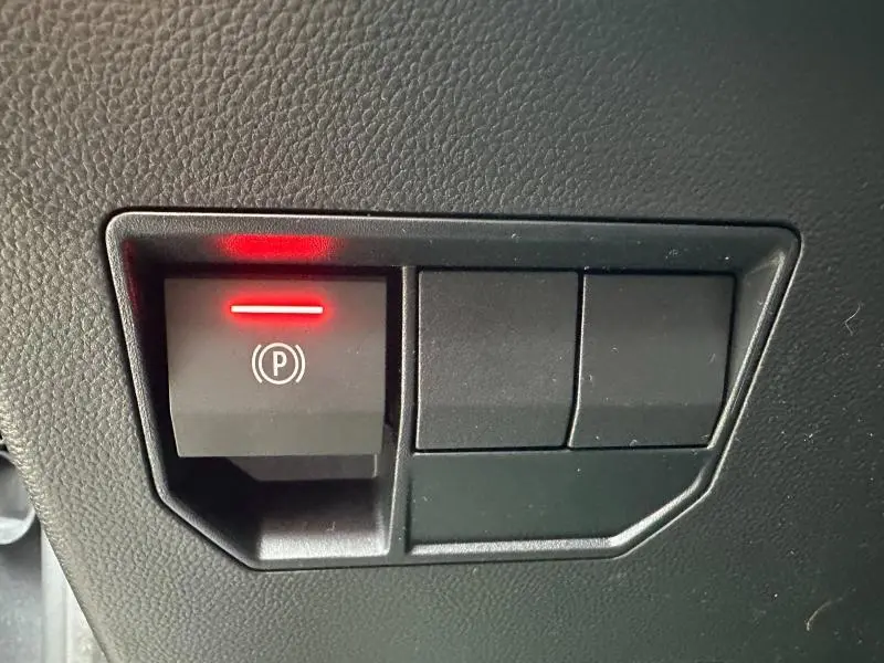 Bouton de frein à main électronique allumé en rouge sur tableau de bord noir du Dacia Duster blanc 2025.