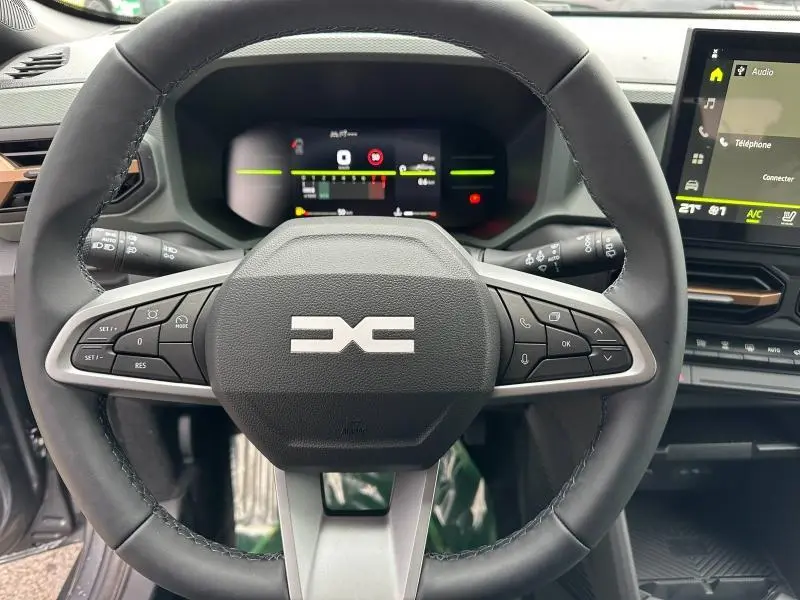 Volant multifonction noir avec logo Dacia, tableau de bord numérique et écran tactile à droite dans un Dacia Duster 2025.
