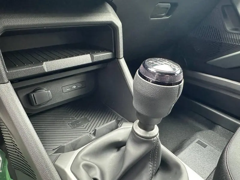 Gros plan sur le levier de vitesses manuel noir du Dacia Duster blanc 2025, avec console centrale et prises USB visibles.