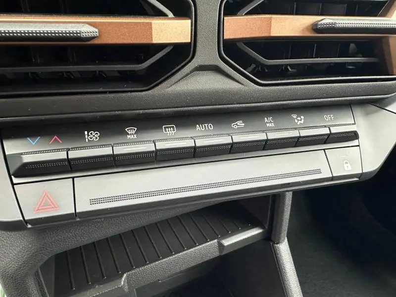 Gros plan sur la console centrale du Dacia Duster 2025 blanc, montrant les commandes de climatisation et les aérateurs noirs avec inserts bronze.