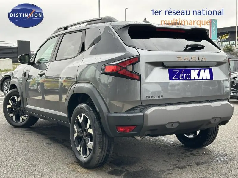 Vue 3/4 arrière droite du Dacia Duster gris avec barres de toit et jantes alliage noires.