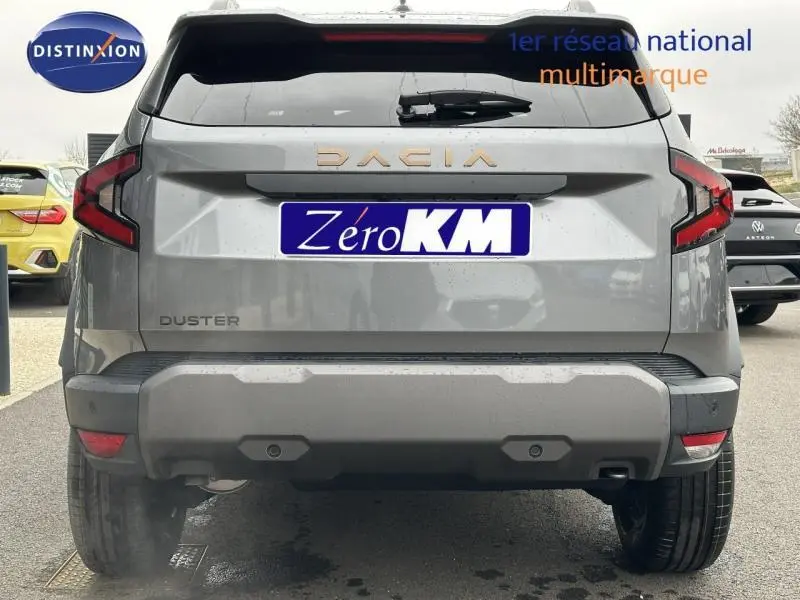 Vue arrière d'un Dacia Duster gris avec feux arrière en forme de C et logo Dacia doré sur le hayon.