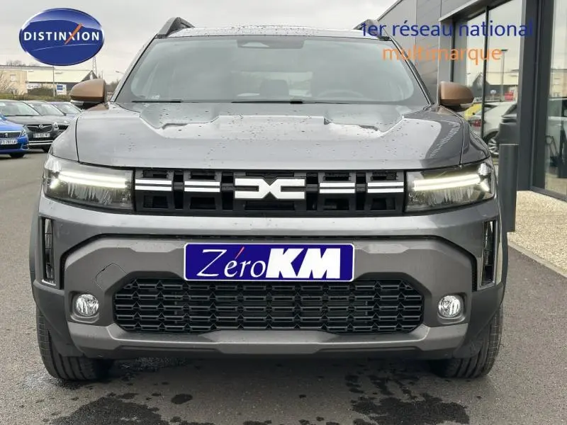 Vue frontale d'un Dacia Duster 2025 gris avec calandre noire et feux LED allumés sur parking.