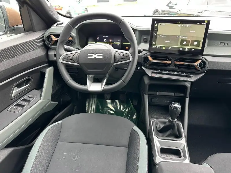 Intérieur du Dacia Duster 2025 blanc, vue du poste de conduite avec volant multifonction et écran tactile central.