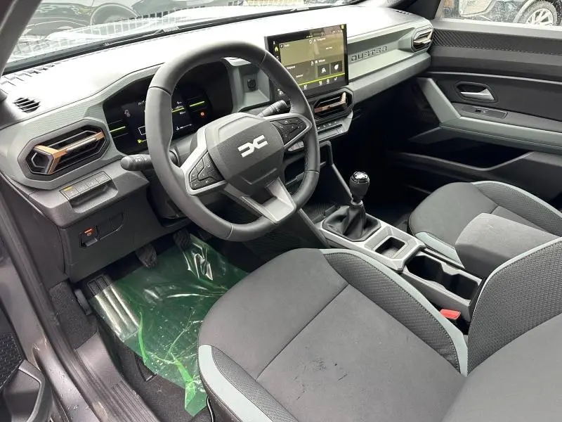 Intérieur du Dacia Duster 2025 vu côté conducteur, volant multifonction, écran tactile et sièges gris foncé.