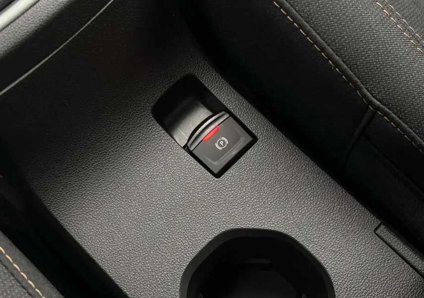 Gros plan sur le frein de parking électrique noir avec témoin rouge, entouré de sellerie gris foncé à surpiqûres contrastées.