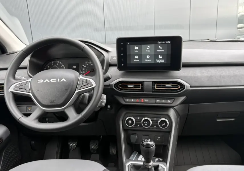 Vue intérieure frontale du tableau de bord et volant Dacia Sandero Stepway 2025, avec écran tactile et levier de vitesses manuel.