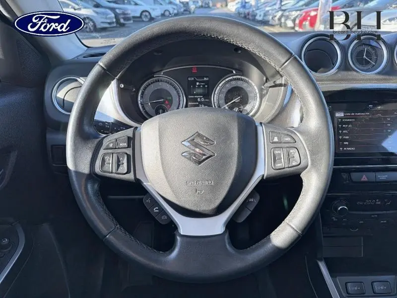 Vue rapprochée du volant cuir multifonction noir du Suzuki Vitara 1.4 Boosterjet Hybrid avec tableau de bord et écran tactile.