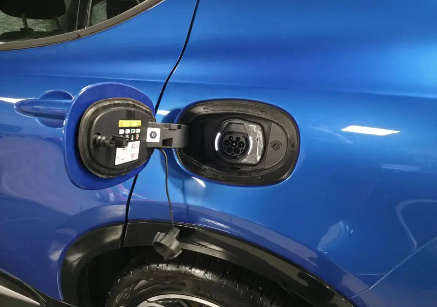 Prise de recharge ouverte côté gauche d’un Alfa Romeo Tonale bleu métallisé, avec jante alliage visible.