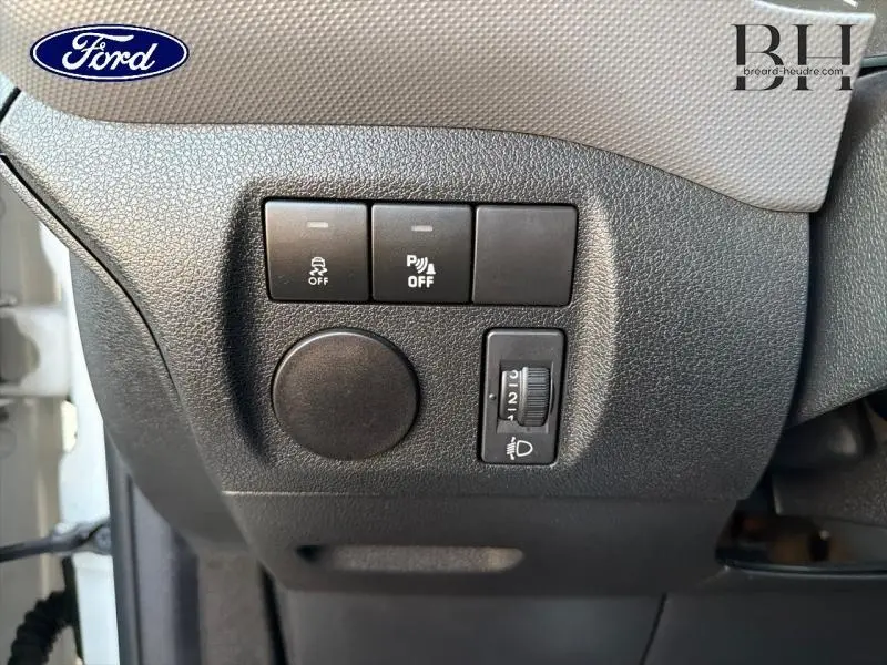 Gros plan sur les commandes de réglage des phares et de l'aide au stationnement dans un Citroën Berlingo blanc, côté conducteur.