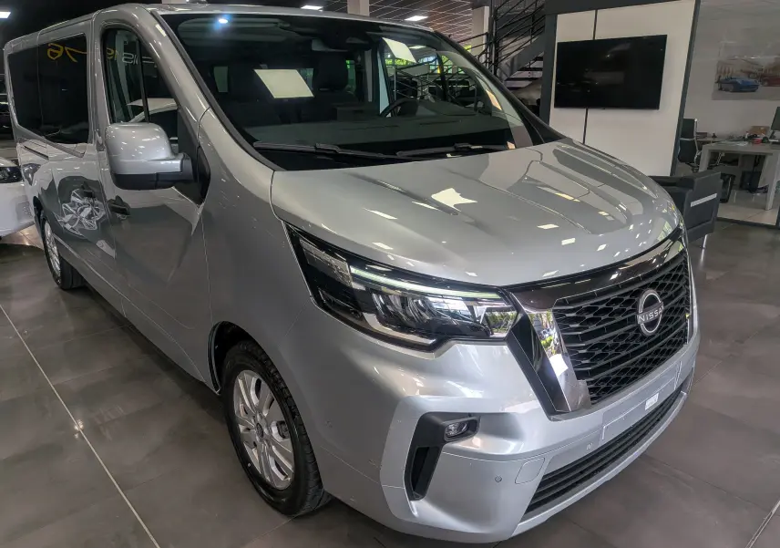 Vue 3/4 avant droite du Nissan Primastar Combi gris Highland 2026 avec calandre noire et phares LED distinctifs.