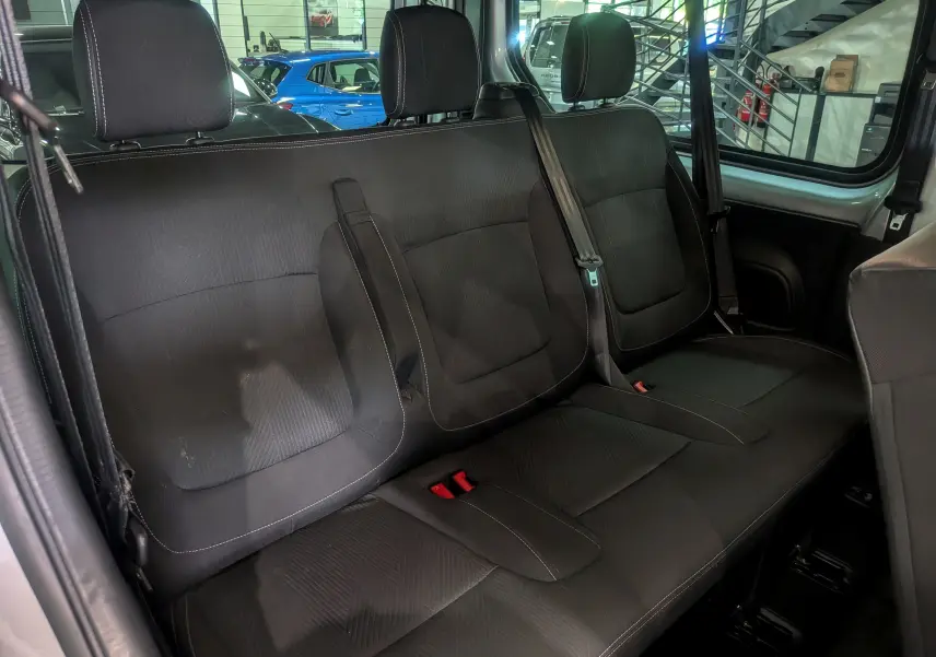 Vue intérieure sur la banquette arrière en tissu noir du Nissan Primastar Combi gris Highland, avec ceintures de sécurité visibles.