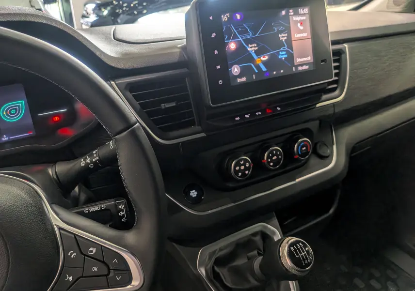 Vue intérieure côté conducteur du Nissan Primastar Combi 2026, tableau de bord noir avec écran tactile et levier de vitesses manuel.