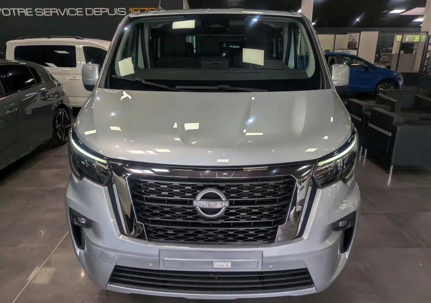 Vue frontale d'un Nissan Primastar Combi gris Highland 2026 avec calandre noire et phares LED allumés.
