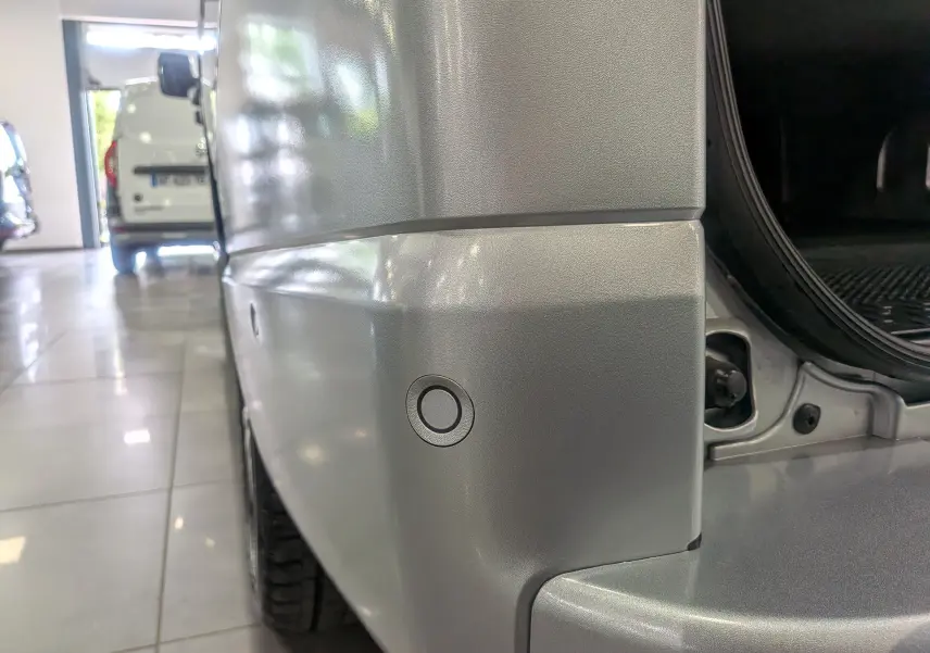 Gros plan sur le pare-chocs arrière droit gris Highland du Nissan Primastar Combi avec capteur de recul visible.