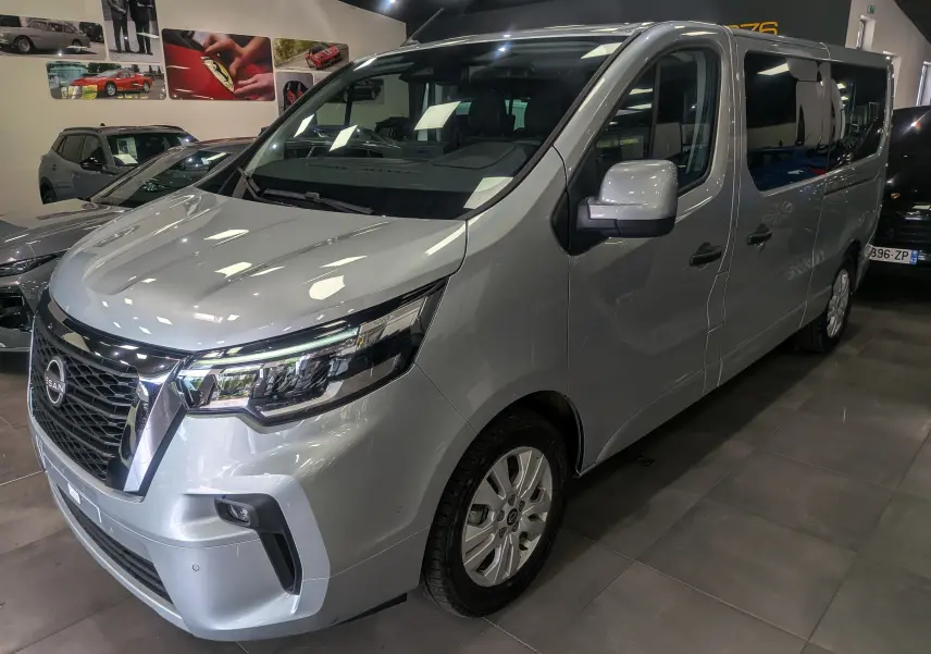 Vue 3/4 avant droite du Nissan Primastar Combi gris Highland 2026 avec calandre noire et vitres teintées.