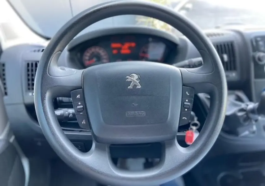 Vue rapprochée du volant Peugeot Boxer Fourgon 2019 avec commandes intégrées et tableau de bord flou en arrière-plan.
