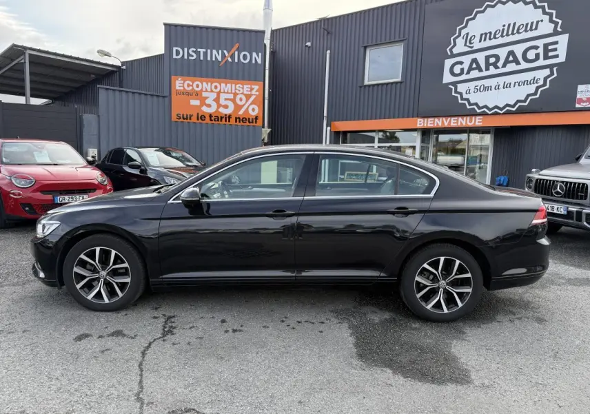 Profil côté gauche d'une Volkswagen Passat noire 2018 garée devant un garage avec jantes alliage visibles.