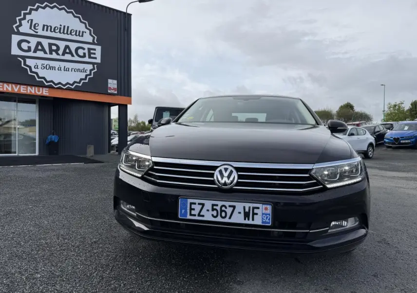 Volkswagen Passat noire vue de face, avec calandre chromée et phares LED allumés sur parking extérieur.