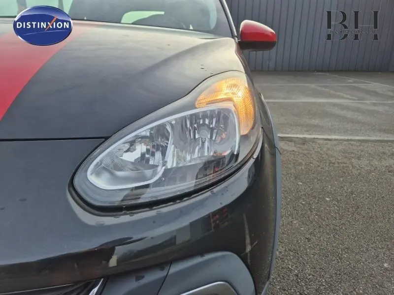 Gros plan sur le phare avant droit allumé d'une Opel Adam Rocks noire avec rétroviseur rouge et bande rouge sur le capot.