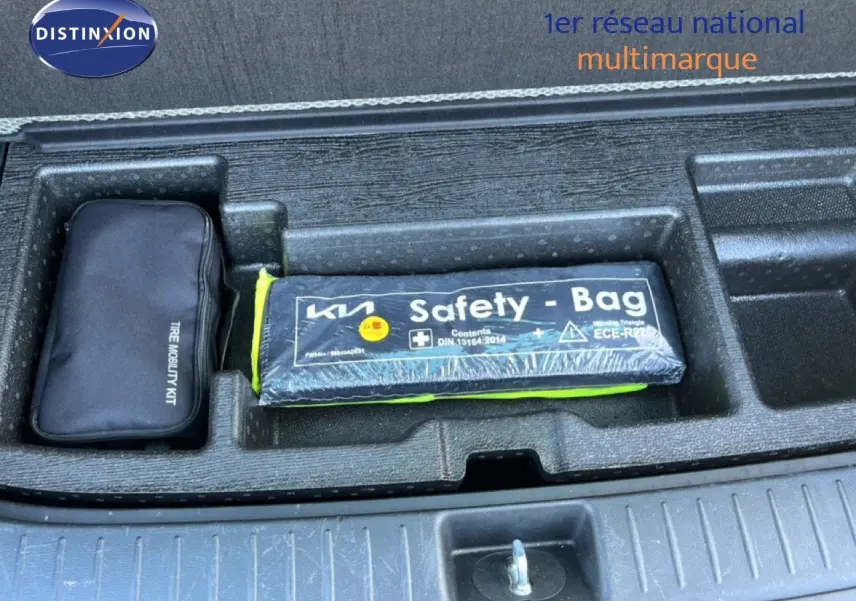 Vue plongeante sur le coffre ouvert d’un Kia Sportage bleu fusion métal, montrant le kit de mobilité et la trousse de sécurité.