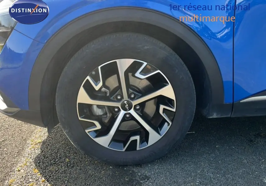 Gros plan sur la roue avant gauche du Kia Sportage bleu fusion métal, mettant en valeur la jante alliage au design moderne.
