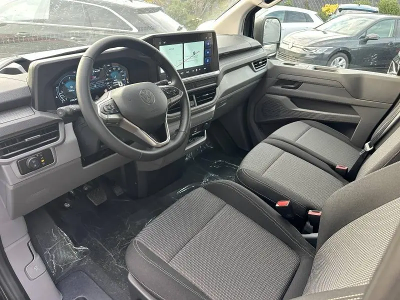 Vue intérieure côté conducteur du Volkswagen Transporter Procab 2025, tableau de bord moderne et sièges tissu gris.