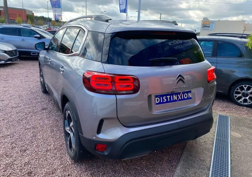 Vue 3/4 arrière d'un Citroën C5 Aircross gris Artense avec feux arrière allumés sur parking extérieur.
